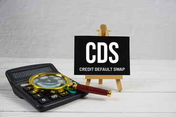CDS abbreviation of Credit Default Swap text with magnifying glass and calculator on wooden...