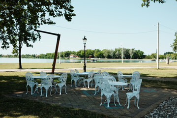 Outdoor white cast iron chairs and tables near Lake Palic, Serbia. Peaceful summer lakeside cafe...