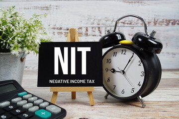 NIT Negative Income Tax text with alarm clock and calculator on wooden background