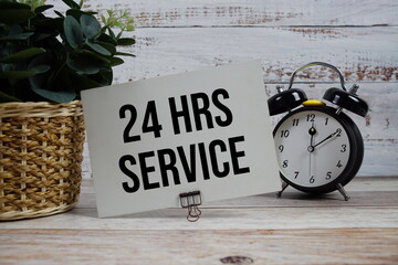 24 HRS. Service text with alarm clock on wooden background
