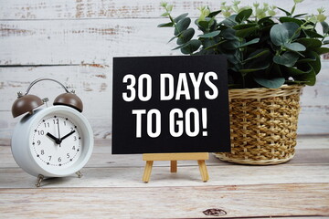 30 Days To Go! text with alarm clock on wooden background