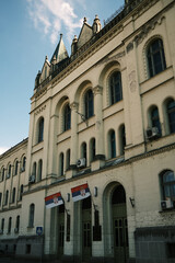 Detailed view of Zrenjanin city hall with Serbian flags and historic architecture. Clear view of arches, windows, and spires under bright daylight. Serbia country.