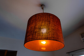 Close-up of a glowing ceiling pendant lamp with a natural straw shade. Warm interior lighting.