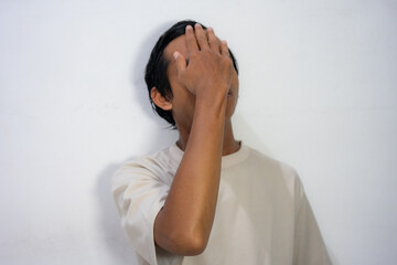 A frustrated young Asian man doing a facepalm gesture, with his hand covering his eyes.
