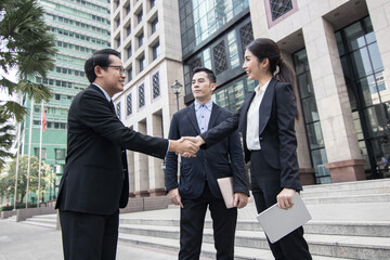 Business investors in suits stand shaking hands outside a building after successful negotiations.