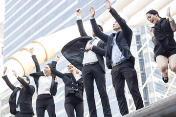 Business investors in suits stand with their hands raised in celebration after achieving their goals outside an office building.