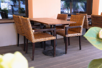 Outdoor cafe seating area with wicker chairs and wooden table, no people, early morning city reflection in window
