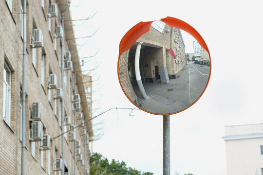Street view with a convex safety mirror reflecting a narrow urban alley and brick building, symbolizing city surveillance, navigation, and visual distortion - Powered by Adobe