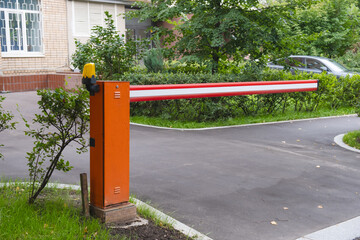 Bright orange security boom gate blocking vehicle access to residential parking area, surrounded by...