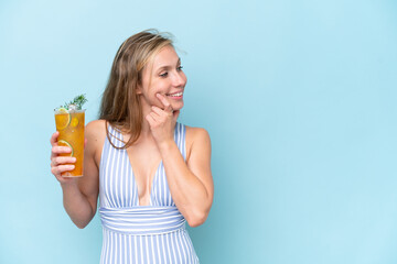 Young blonde woman wearing swimsuit holding a cocktail isolated on blue background thinking an idea...