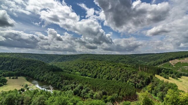 Breathtaking time lapse of lush green forest with rolling hills and winding river. Vibrant blue sky with fluffy clouds creating  picturesque and serene landscape.