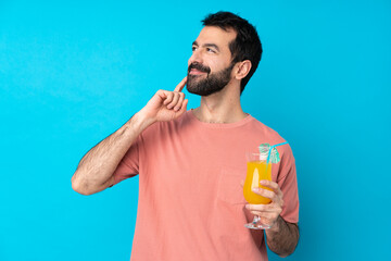 Young man over holding a cocktail over isolated blue background thinking an idea while looking up