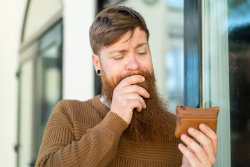 Redhead man with beard holding a wallet and looking it