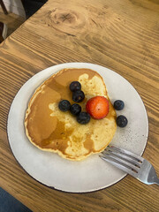 Pancake with fresh blueberries and strawberry on ceramic plate, breakfast on rustic wooden table