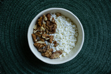White cup with cottage cheese and walnuts on green background, top view