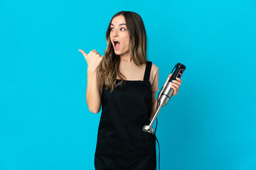 Romanian woman using hand blender isolated on blue background intending to realizes the solution...