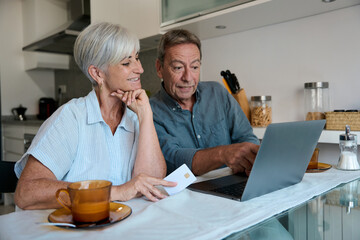 Senior couple making online payment using laptop and credit card in kitchen