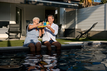 Senior couple toasting cocktails by the poolside at home