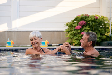 Happy senior couple holding hands and having fun in swimming pool