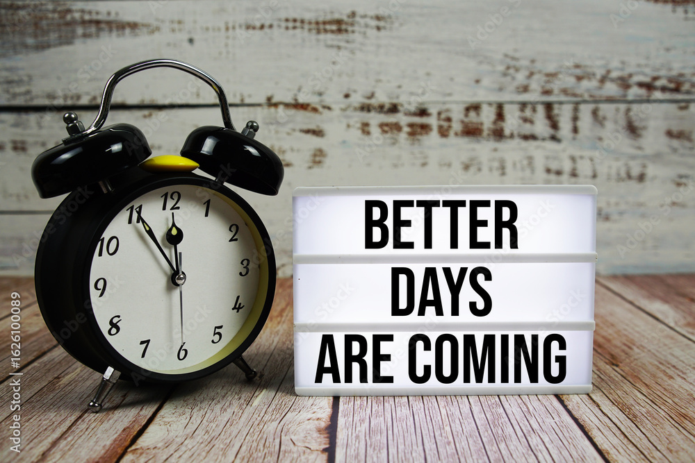 Poster better days are coming text on light box with alarm clock on wooden background