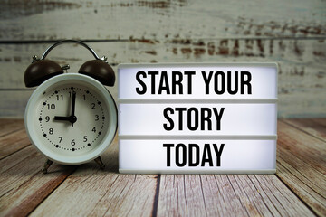Start Your Story Today text on light box with alarm clock on wooden background