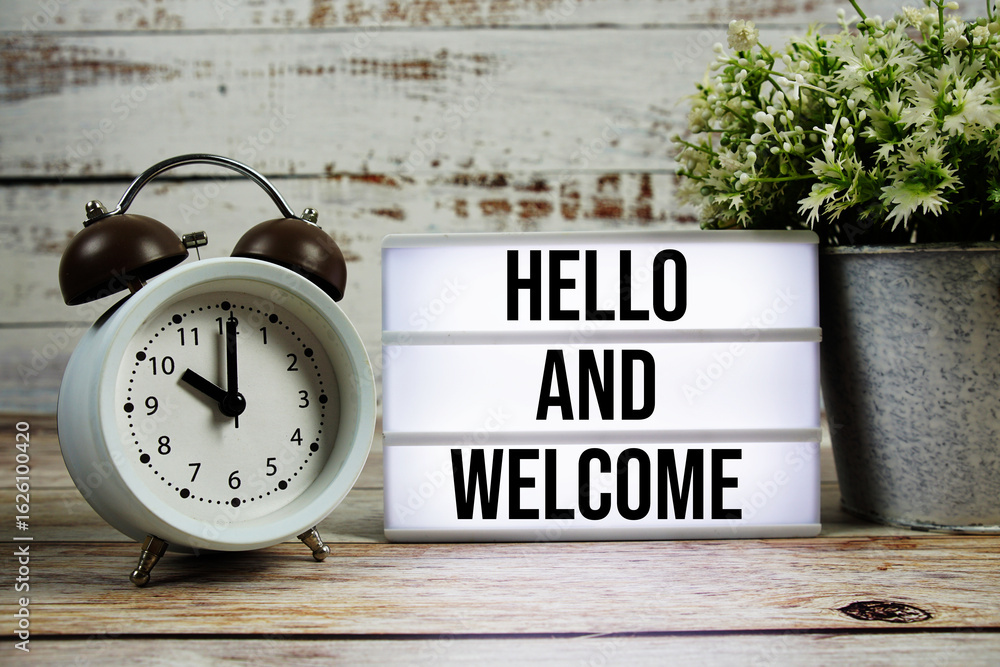 Poster hello and welcome text on light box with alarm clock on wooden background