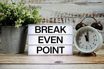 Break even point text on light box with alarm clock on wooden background