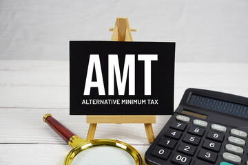 AMT Alternative Minimum Tax text with magnifying glass and calculator on wooden background