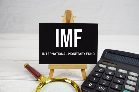 IMF International Monetary Fund text with magnifying glass and calculator on wooden background