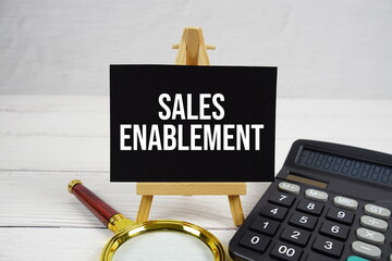 Sales Enablement text with magnifying glass and calculator on wooden background