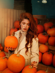 Beautiful red-haired young woman with orange pumpkin in her hands walks through the city autumn vegetable market. Autumn and Halloween season.