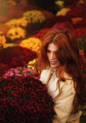 Beautiful red-haired young woman with a bouquet of autumn chrysanthemum flowers at the city flower market.