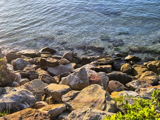 Rugged, textured and eroded stones form a slope from the land to the water's edge. Clear water...