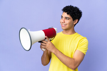 Young Venezuelan man isolated on purple background shouting through a megaphone to announce...