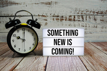 Something New Is Coming! text on light box with alarm clock on wooden background