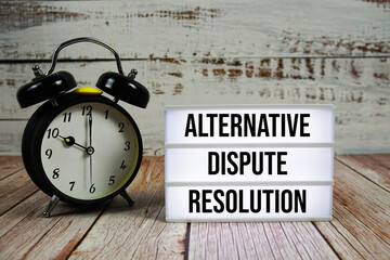 ADR Alternative Dispute Resolution text on light box with alarm clock on wooden background