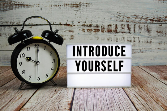 Introduce Yourself text on light box with alarm clock on wooden background