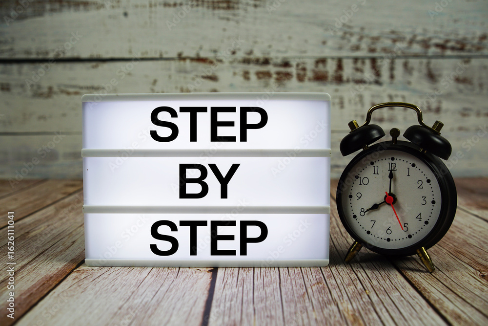 Poster step by step text on light box with alarm clock on wooden background