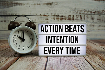 Action beats intention every time text on light box with alarm clock on wooden background