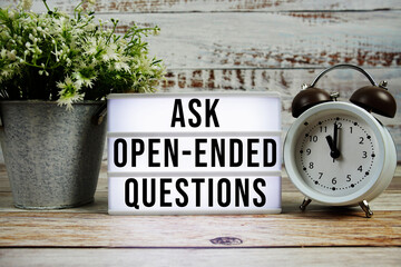 Ask Open-Ended Questions text on light box with alarm clock on wooden background