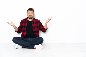 Young handsome man sitting on the floor with shocked facial expression