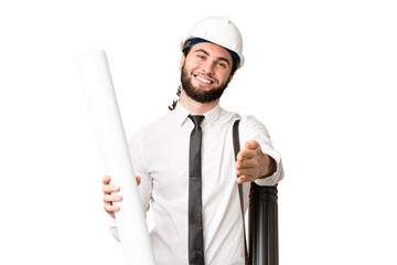 Young architect man with helmet and holding blueprints over isolated chroma key background shaking...