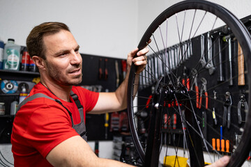Experienced bicycle serviceman balancing and centering wheel in bike shop.