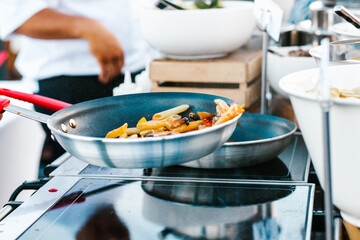 Chef cooking pasta and vegetables in a frying pan