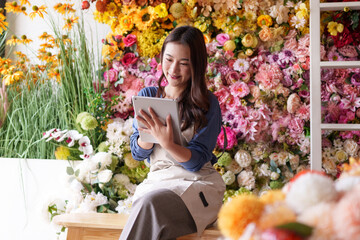 Asian adult woman manages artificial flower shop using digital tablet for online sales entrepreneur...