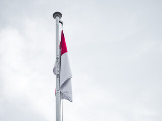 Indonesian flag waving on a tall pole against a cloudy sky, symbolizing national pride,...
