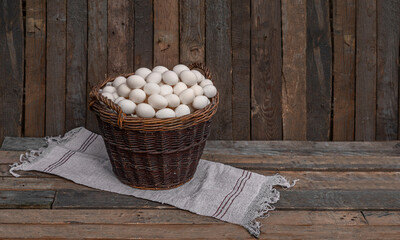 Chicken eggs in large wicker basket with wall of chicken coop, barn or wooden grunge fence in the...