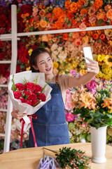 Asian adult florist entrepreneur taking selfie with red rose bouquet showcasing beautiful...