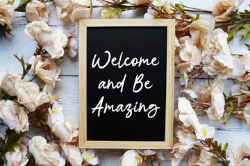 Welcome and Be Amazing text with flower decoration on wooden background