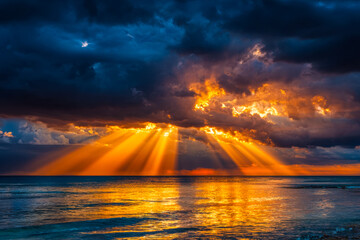 Stunning sunset over the ocean with dramatic cloud formations and golden sun rays breaking through the clouds